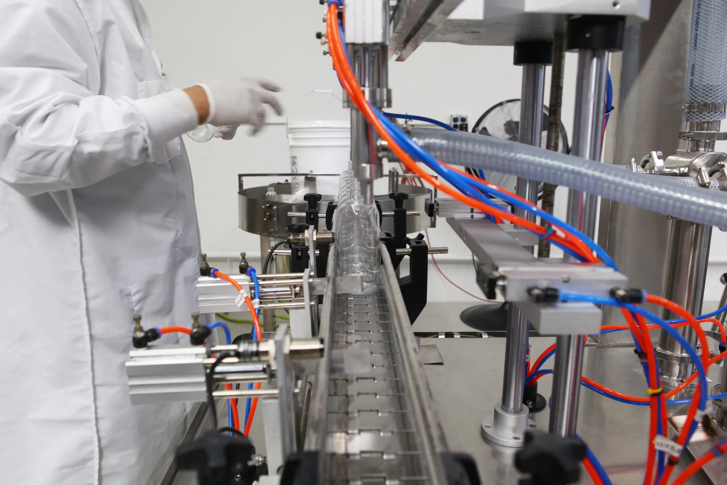 A filling line at the Formology Lab plant in Chatsworth: an operator in a white coat and gloves beside a conveyor of clear bottles.